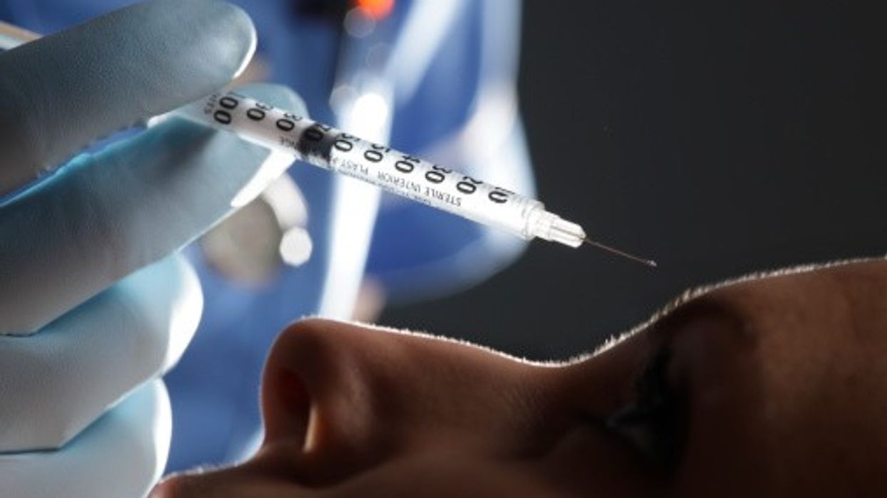 Gloved medic holding syringe near patient’s face for cosmetic injection