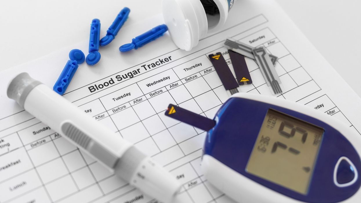 Glucose monitor and test strips on a blood sugar tracker sheet with lancets and pen device.