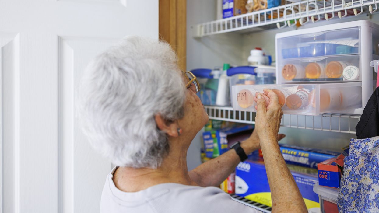 Older adult organizing medicine bottles in a cool, dry storage area during warm weather.